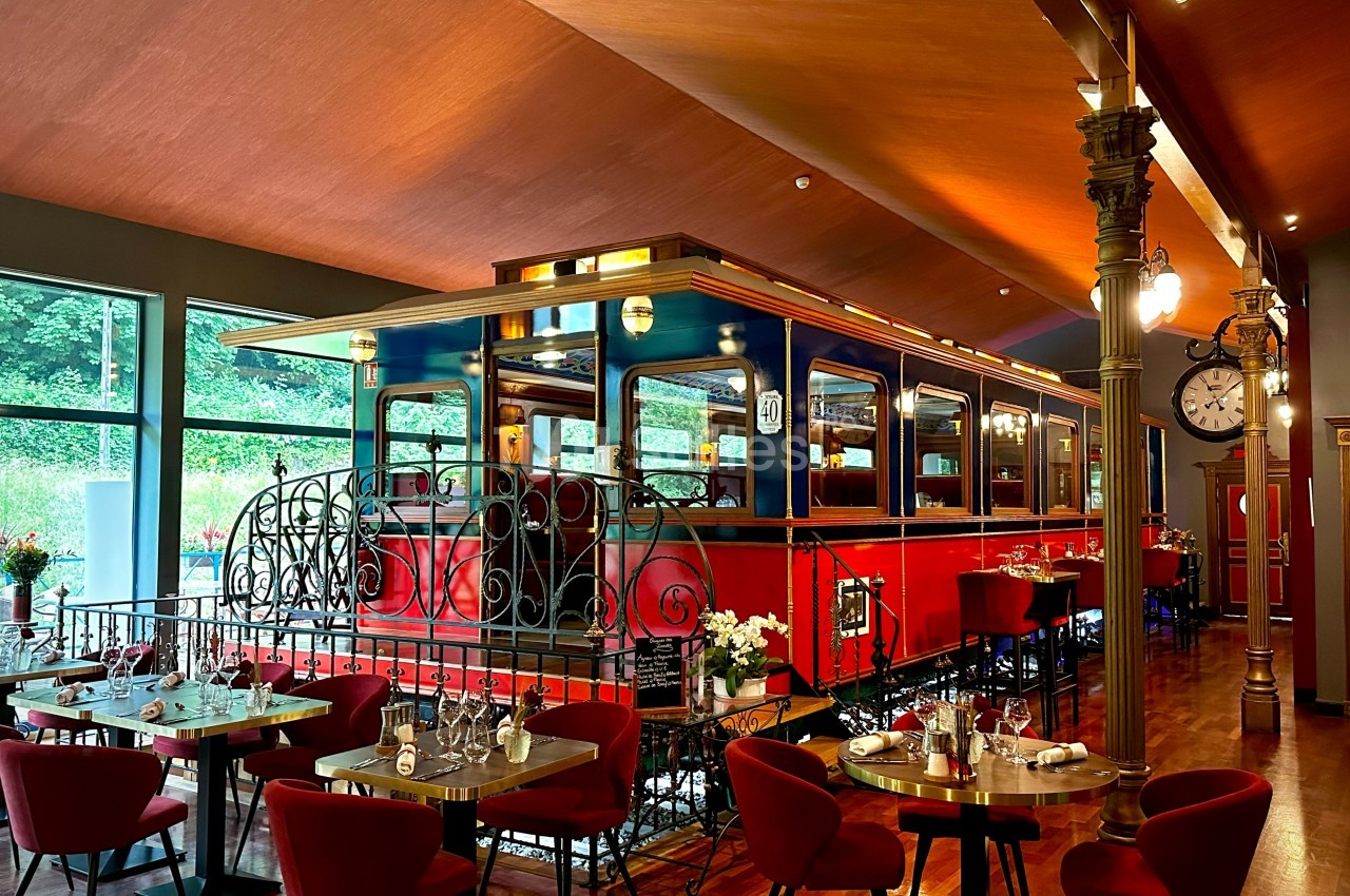 Wagon de train rouge aménagé en salle de restaurant, entouré de tables dressées dans un décor chaleureux.