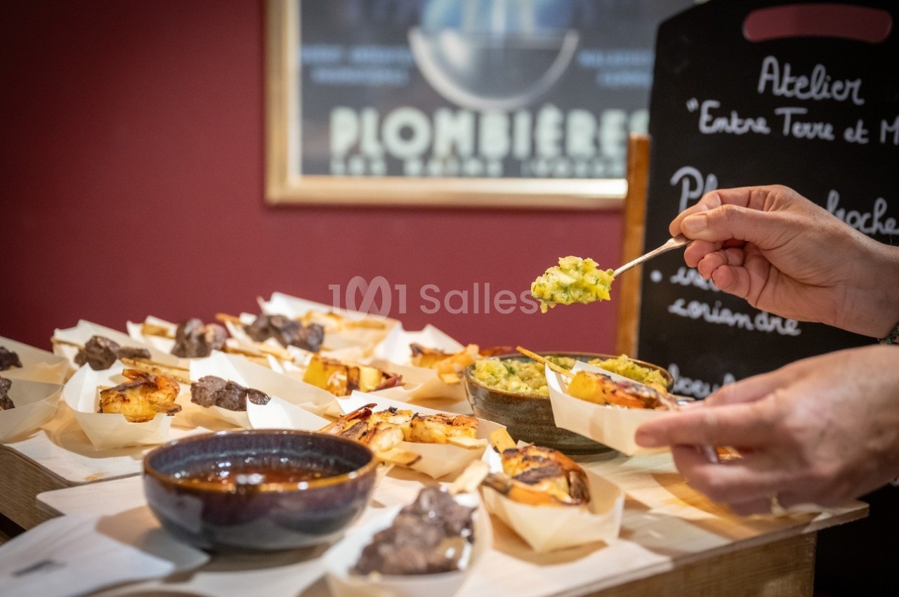 Assortiment de plats et amuse-bouches présentés sur une table, une main servant une préparation avec une cuillère.