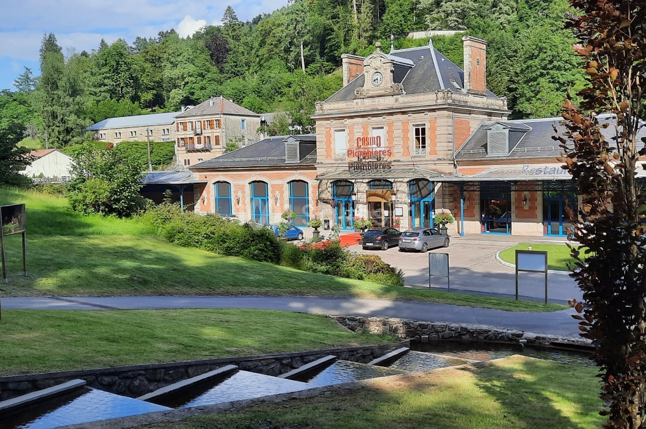 Bâtiment en briques rouges avec horloge, entouré de verdure, situé près d'un ruisseau et d'une pente herbeuse.