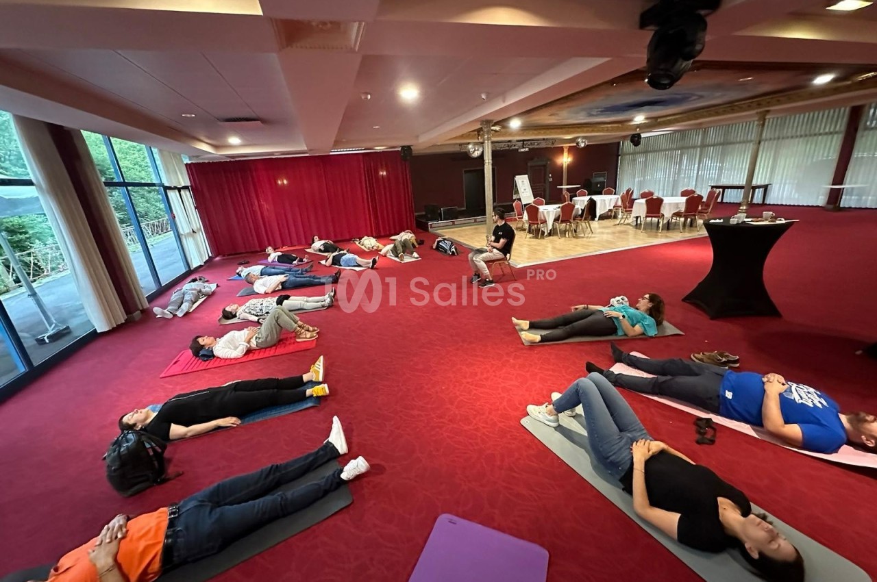 Personnes allongées sur des tapis dans une salle avec moquette rouge, participant à une séance de relaxation ou de…
