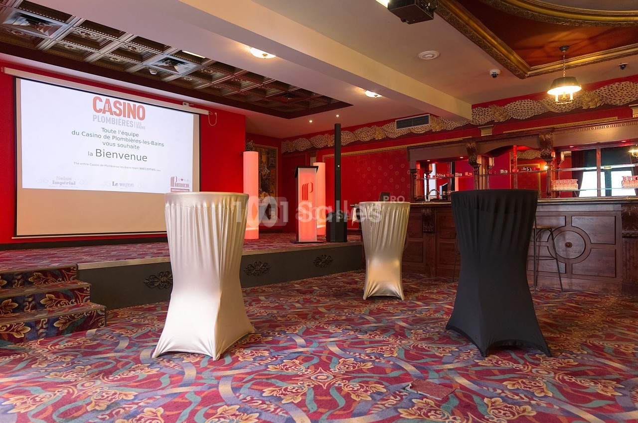 Salle de réception avec tables hautes drapées, écran de projection et décorations de style classique.