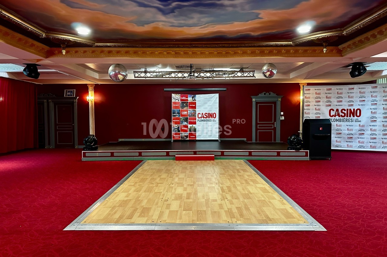 Salle de spectacle avec scène surélevée, parquet central, plafond peint et décorations rouges et dorées.
