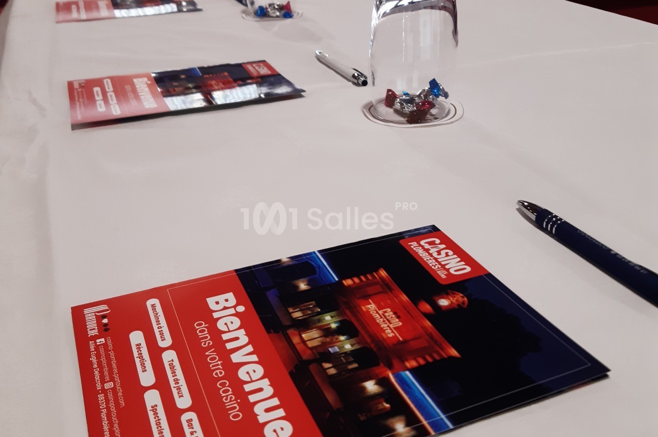Brochures d'un casino posées sur une table blanche avec des stylos, un verre d'eau et des bonbons.