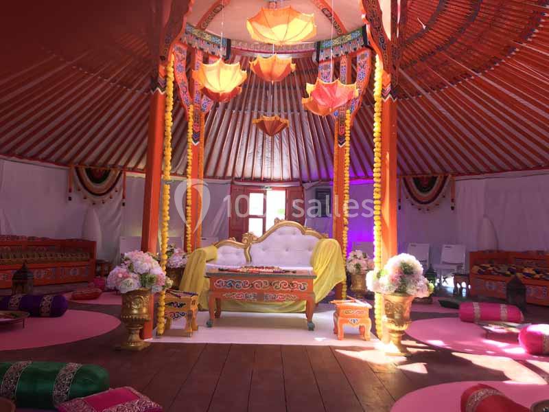 Intérieur d'une tente décorée avec des motifs colorés, un canapé central, des coussins au sol et des luminaires suspendus.