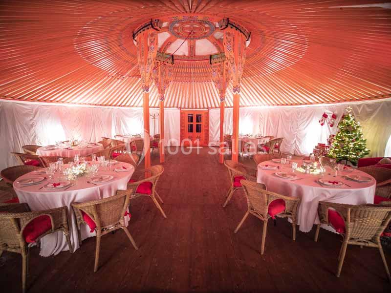 Salle circulaire décorée avec des tables dressées, des chaises en osier et un sapin de Noël illuminé dans un coin.