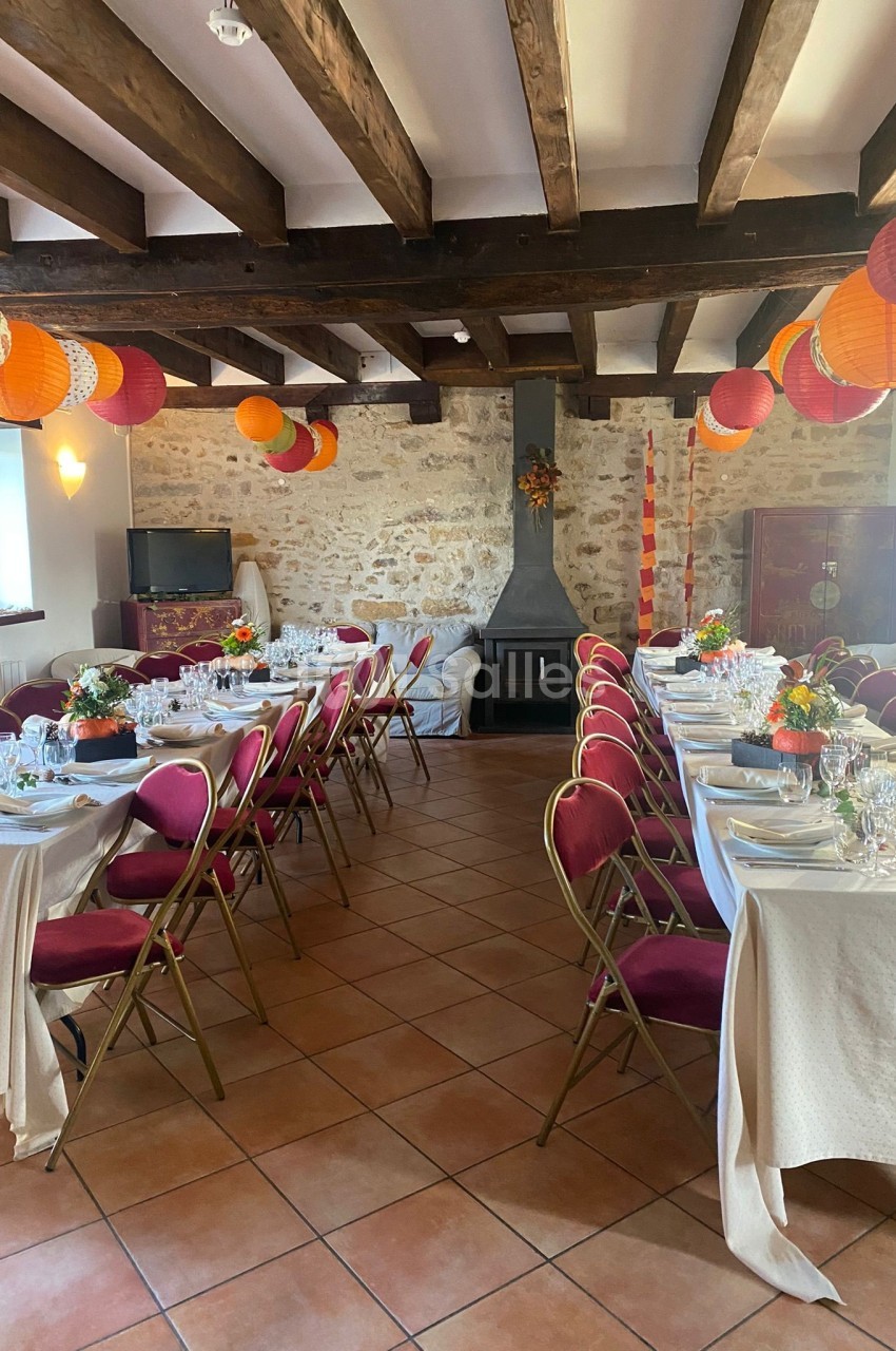 Salle de réception décorée avec des tables dressées, des chaises rouges et des lanternes suspendues sous un plafond en…