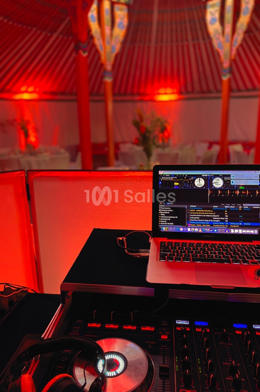 Poste de DJ avec ordinateur portable, table de mixage et casque, dans une salle décorée de lumières rouges.