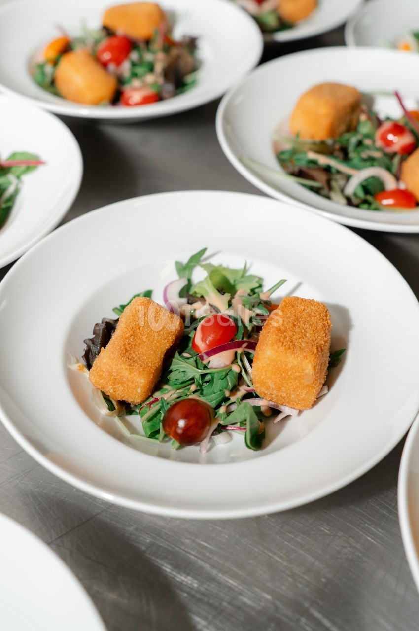 Assiette de salade garnie de tomates cerises, feuilles vertes et deux croquettes dorées.