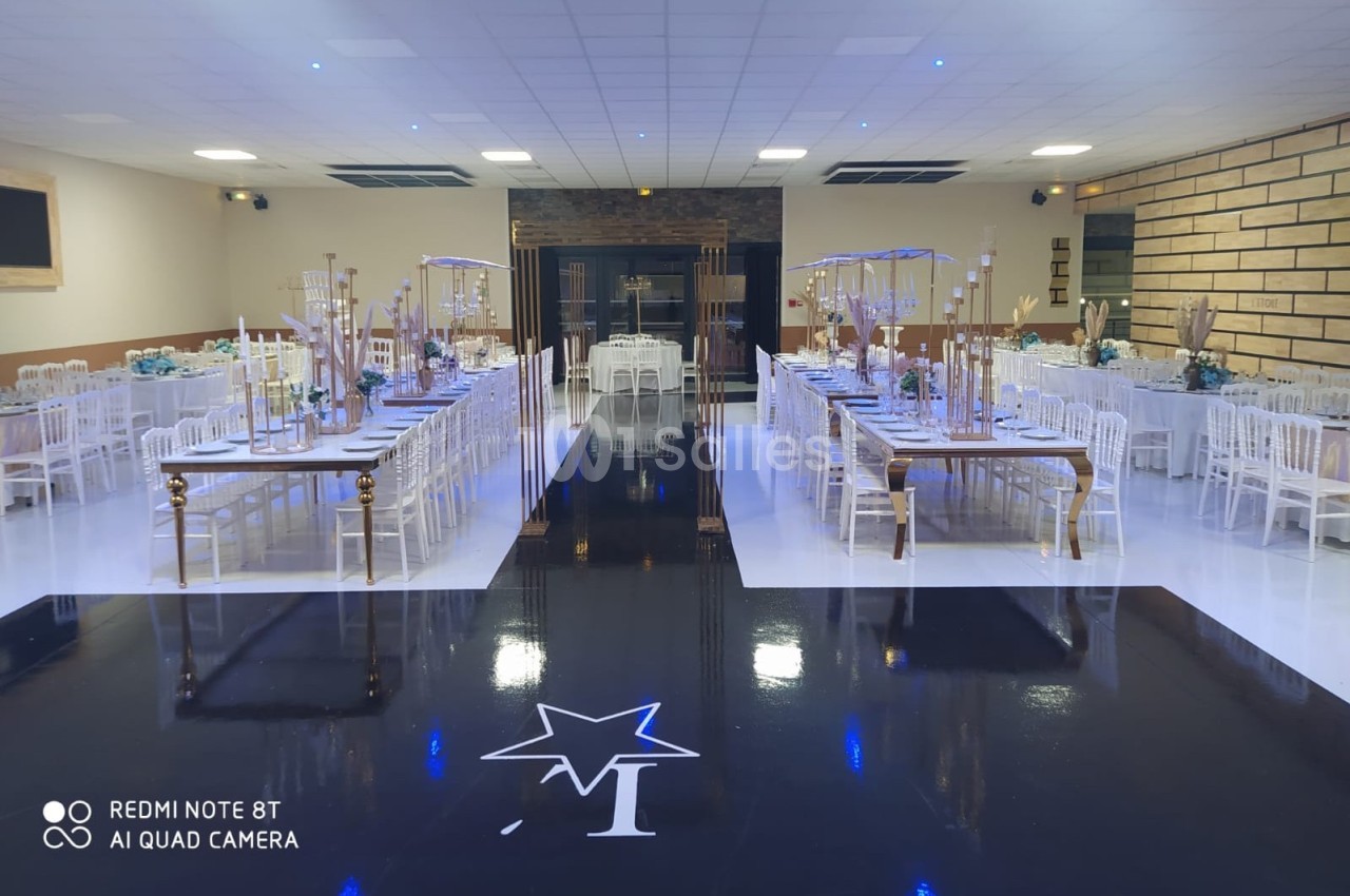 Salle de réception décorée avec des tables alignées, des chaises blanches et une piste noire centrale ornée d'une étoile.