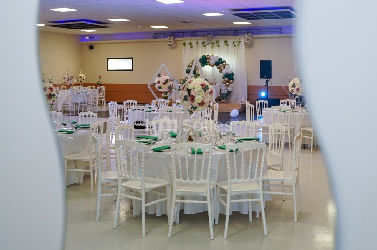 Salle de réception décorée avec des tables rondes, nappes blanches, chaises assorties et ornements floraux.