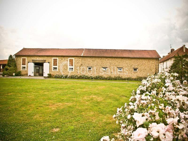 Bâtiment en pierre avec toit en tuiles rouges, entouré d'une pelouse et de rosiers en fleurs au premier plan.