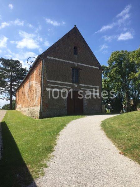 Bâtiment en briques anciennes avec une porte en bois, situé au bout d'un chemin gravillonné entouré de verdure.