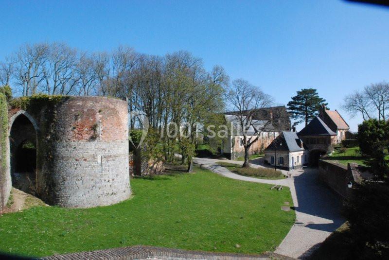 Vue d'un parc avec des ruines en briques, des arbres, un chemin pavé et des bâtiments anciens sous un ciel bleu.