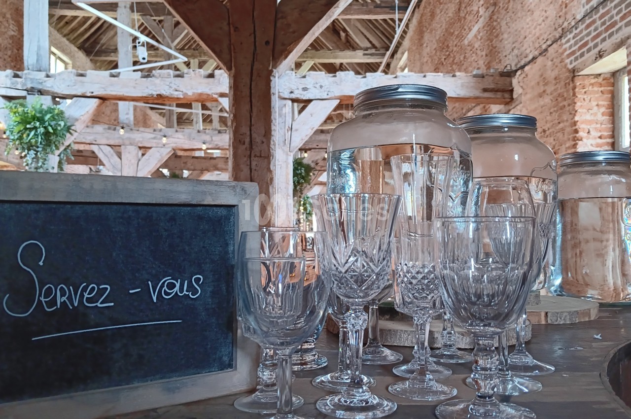 Verres en cristal et bocaux en verre disposés sur une table en bois, avec une ardoise indiquant ’Servez-vous’.