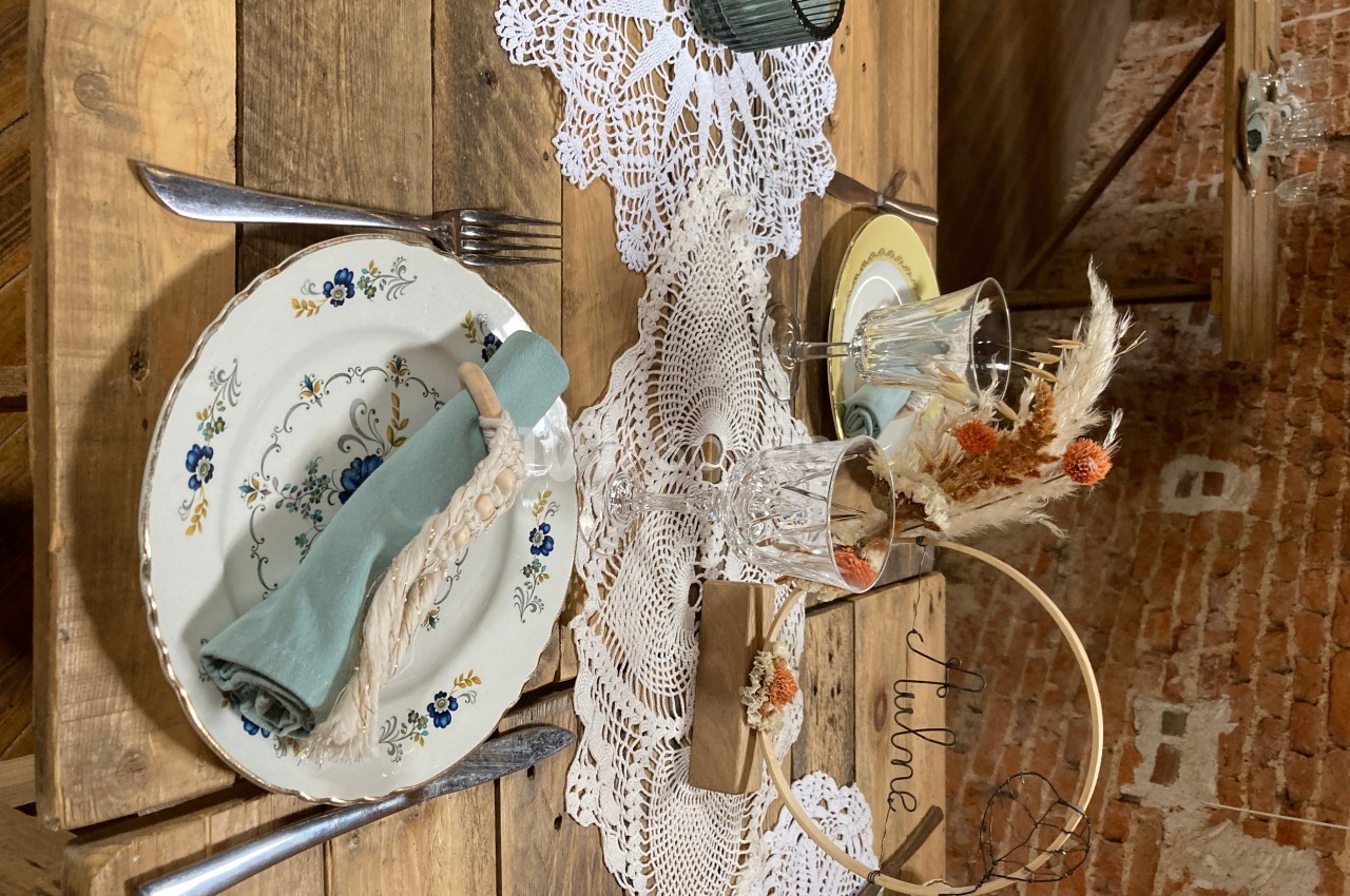 Table en bois décorée avec des assiettes fleuries, un chemin de table en dentelle et des éléments de décoration champêtre.