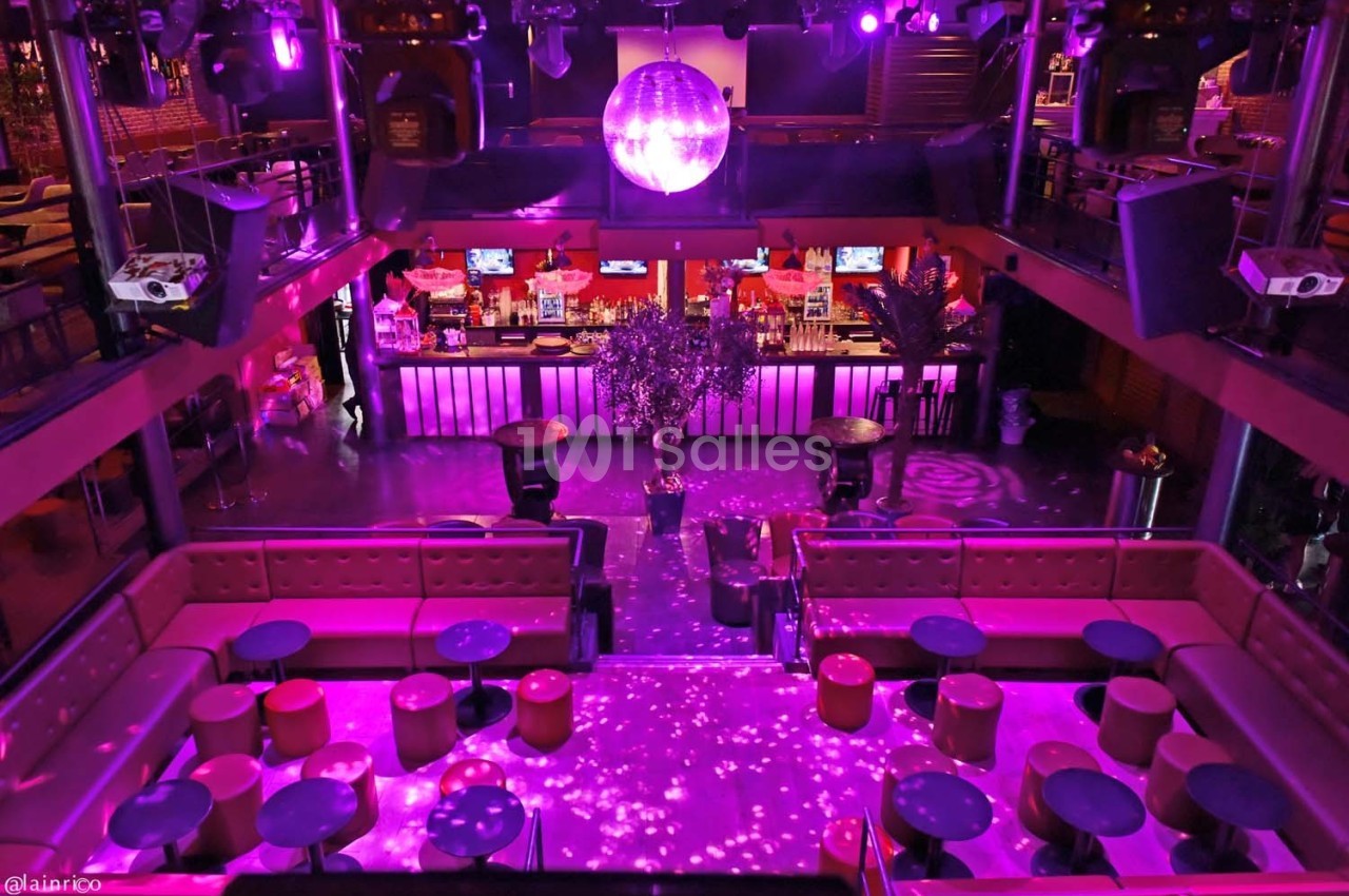 Vue intérieure d'une discothèque avec éclairage violet, piste de danse, banquettes rouges et bar illuminé en arrière-plan.