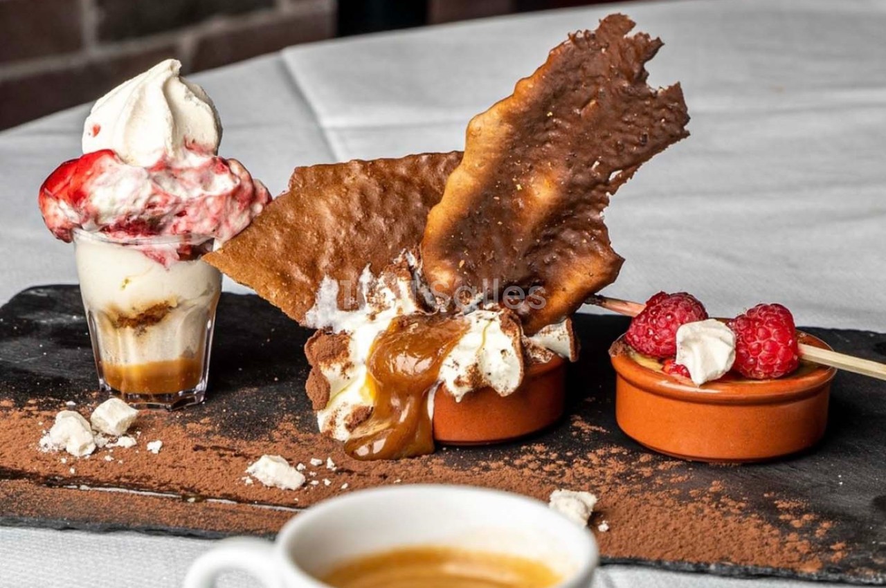Dessert composé de crème glacée, framboises, chocolat, meringue et caramel, présenté sur une ardoise avec un café.