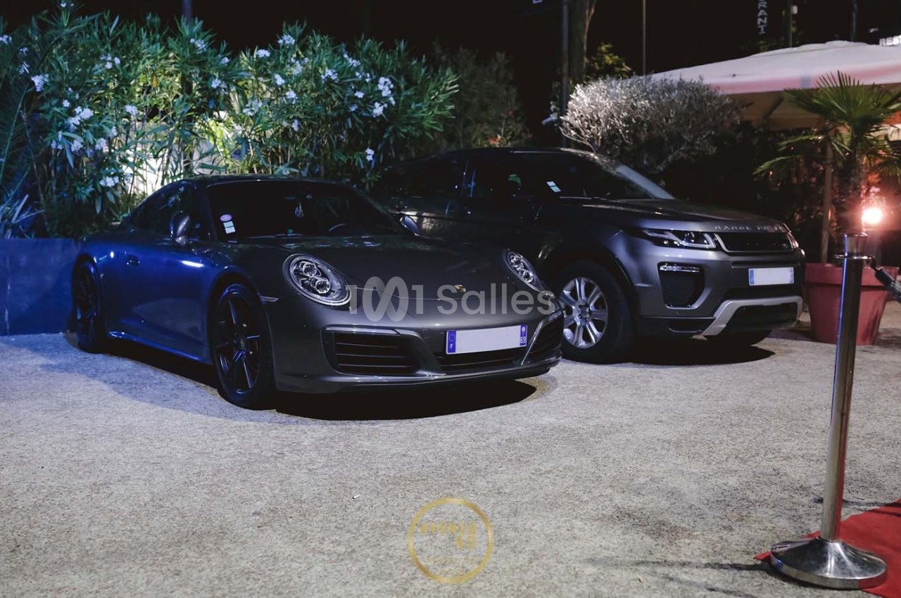 Deux voitures de luxe, une sportive grise et un SUV gris foncé, stationnées côte à côte en extérieur de nuit.