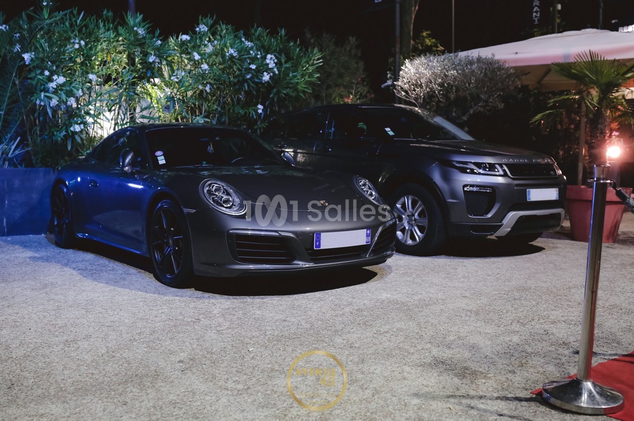 Deux voitures stationnées de nuit, une Porsche grise et un SUV Range Rover, entourées de végétation et d'éclairage urbain.
