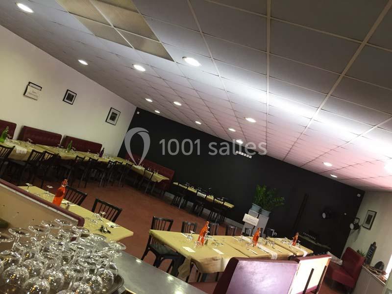 Salle de restaurant avec tables dressées, chaises noires, murs clairs et une décoration sobre.