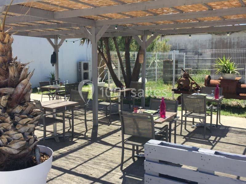 Terrasse extérieure ombragée avec tables et chaises, entourée de végétation et d'éléments décoratifs en métal.