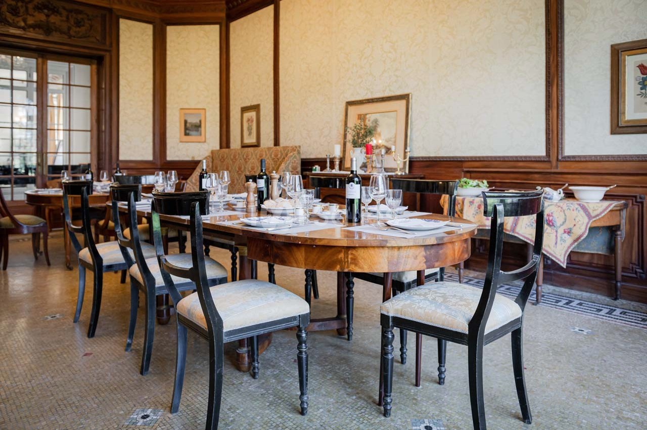 Salle à manger élégante avec tables en bois dressées, chaises rembourrées et décoration classique sur les murs.