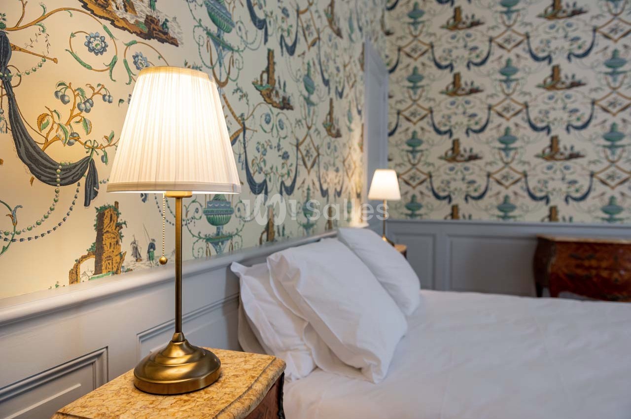 Lampe de chevet allumée sur une table en marbre près d'un lit avec des oreillers blancs, décor mural à motifs.