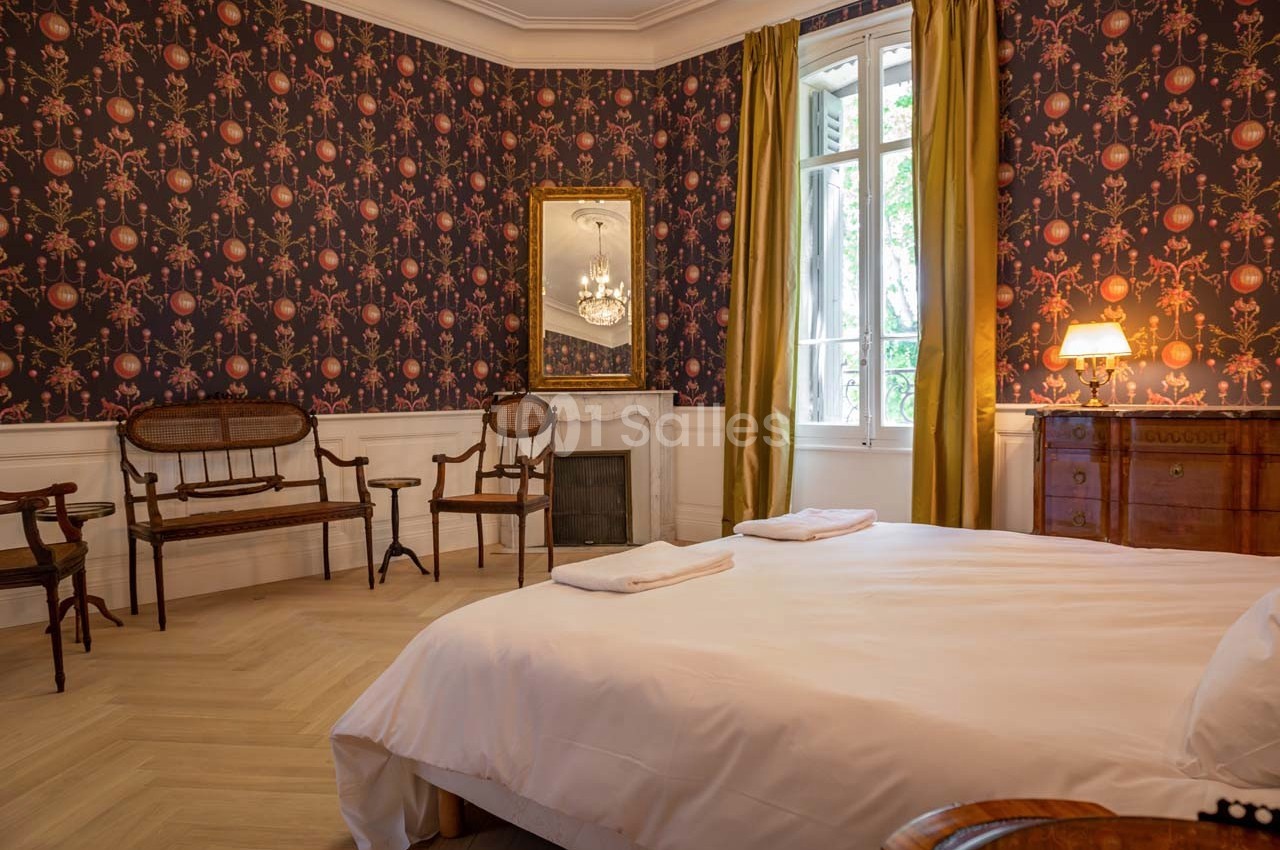 Chambre avec lit double, mobilier en bois ancien, cheminée, miroir, et fenêtre avec rideaux jaunes.