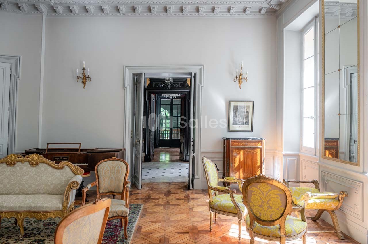Salon élégant avec parquet en bois, mobilier classique, moulures au plafond et vue sur un couloir lumineux.