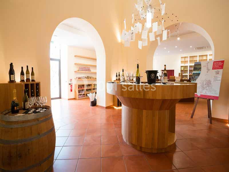 Salle lumineuse avec comptoir en bois, bouteilles de vin exposées, tonneau décoratif et présentoirs en arrière-plan.