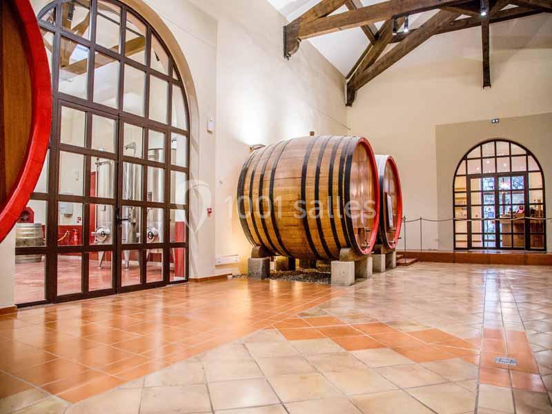 Salle de vieillissement avec de grands tonneaux en bois, sol en carrelage et poutres apparentes au plafond.