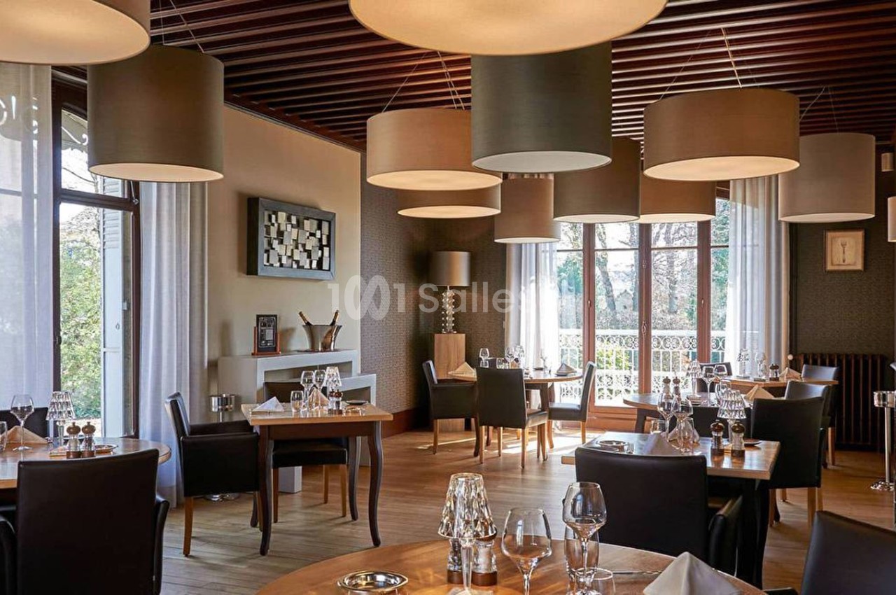 Salle de restaurant élégante avec tables dressées, grandes baies vitrées et suspensions lumineuses modernes.