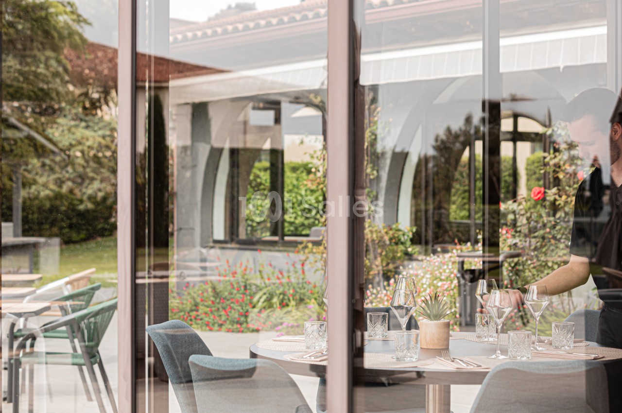 Un serveur prépare une table élégamment dressée dans un restaurant avec vue sur un jardin fleuri.