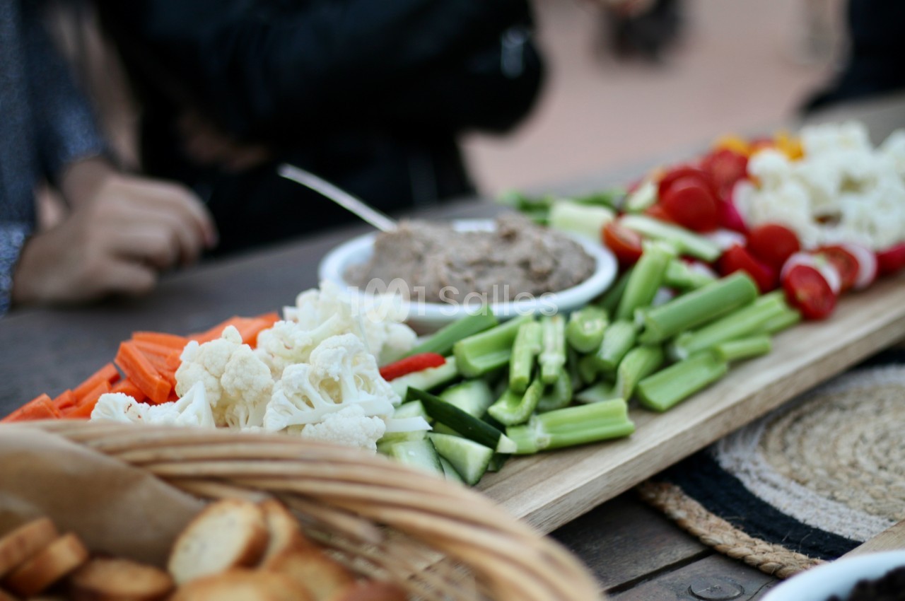 Plateau de crudités variées avec carottes, chou-fleur, concombres et tomates, accompagné d'une sauce dans un bol.