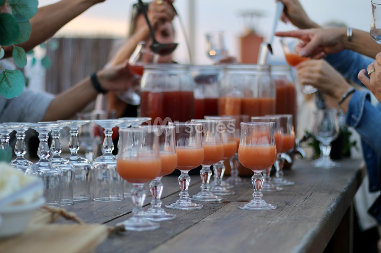 Des verres de cocktail orange disposés sur une table en bois, entourés de mains servant des boissons.