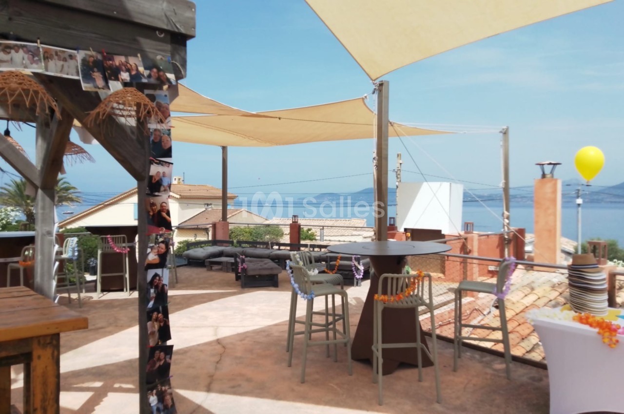 Terrasse ensoleillée avec des voiles d'ombrage, mobilier de jardin et vue sur la mer et les toits environnants.