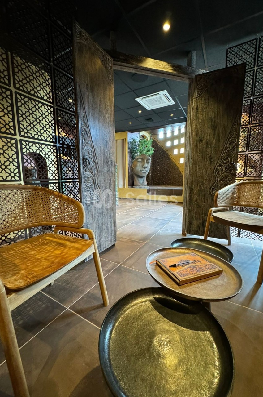 Salle d'attente au style asiatique avec chaises en rotin, tables basses et décoration murale sculptée.