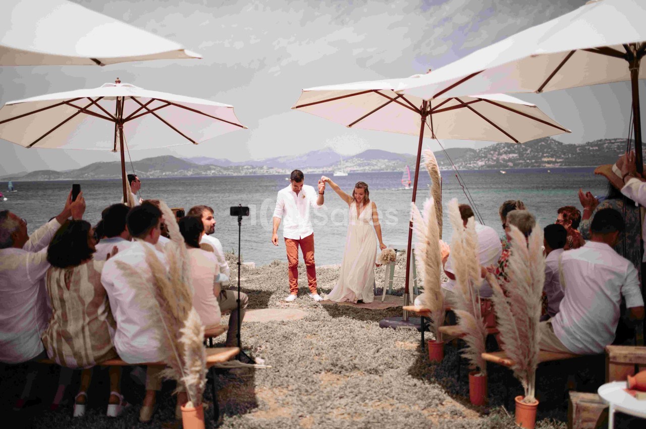 Un couple se tenant la main lors d'une cérémonie de mariage en plein air, près de la mer, sous des parasols.