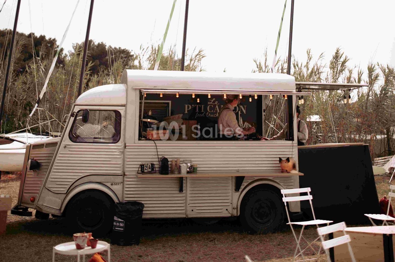 Camion-restaurant vintage stationné en extérieur, avec un cuisinier préparant des plats derrière le comptoir.