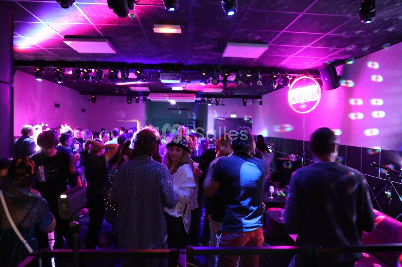 Personnes dansant et discutant dans une salle de club éclairée par des lumières colorées et un logo lumineux au mur.