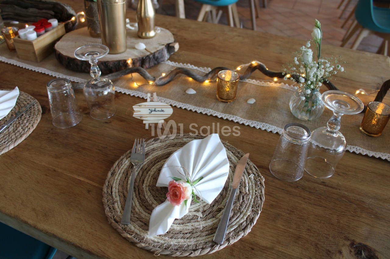 Table décorée pour un repas avec sets en corde, serviettes pliées, fleurs, bougies et guirlande lumineuse.