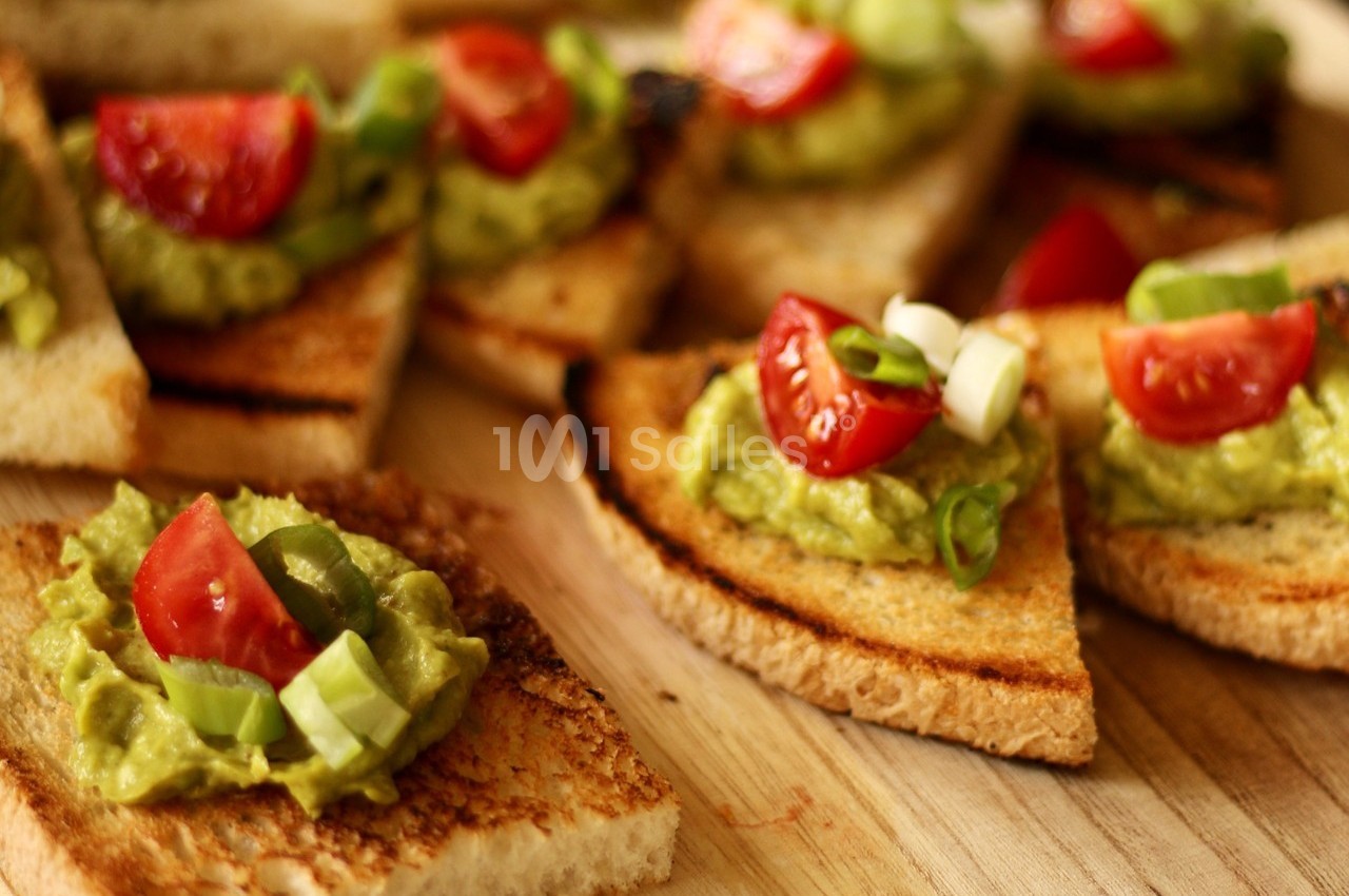 Tranches de pain grillé garnies de guacamole, de tomates cerises et de rondelles d'oignons verts.