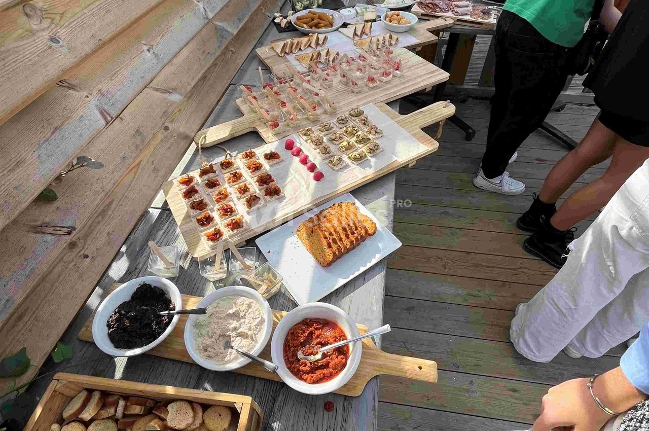Buffet en extérieur avec divers amuse-bouches, tartinades, pain et condiments disposés sur des planches en bois.