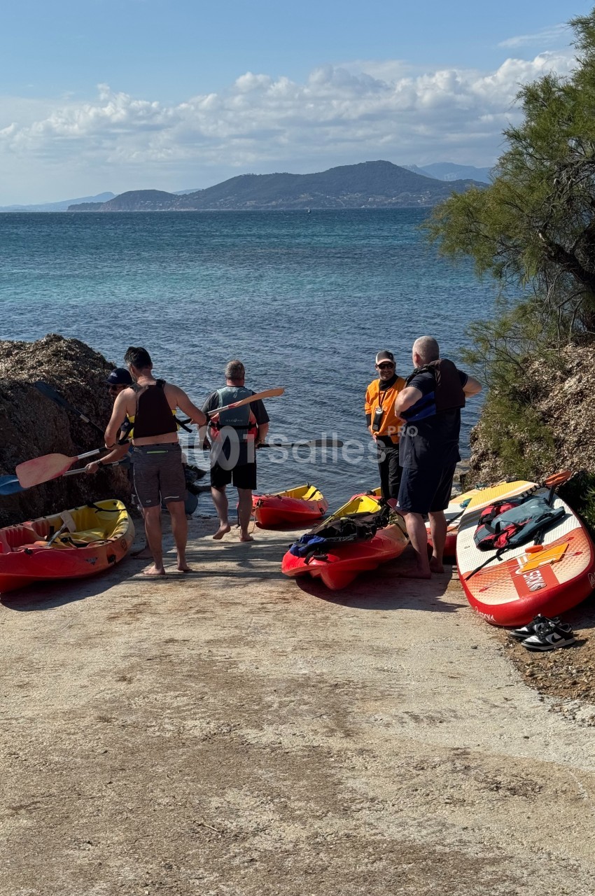 Des personnes préparent des kayaks sur une rampe en bord de mer, avec une vue sur des collines à l'horizon.