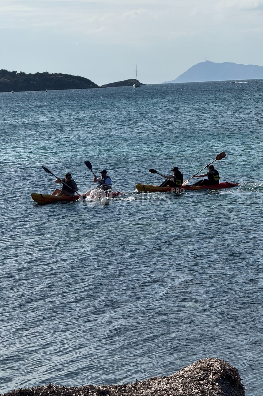 Quatre personnes pagayant sur deux kayaks doubles dans une mer calme, avec des îles en arrière-plan.