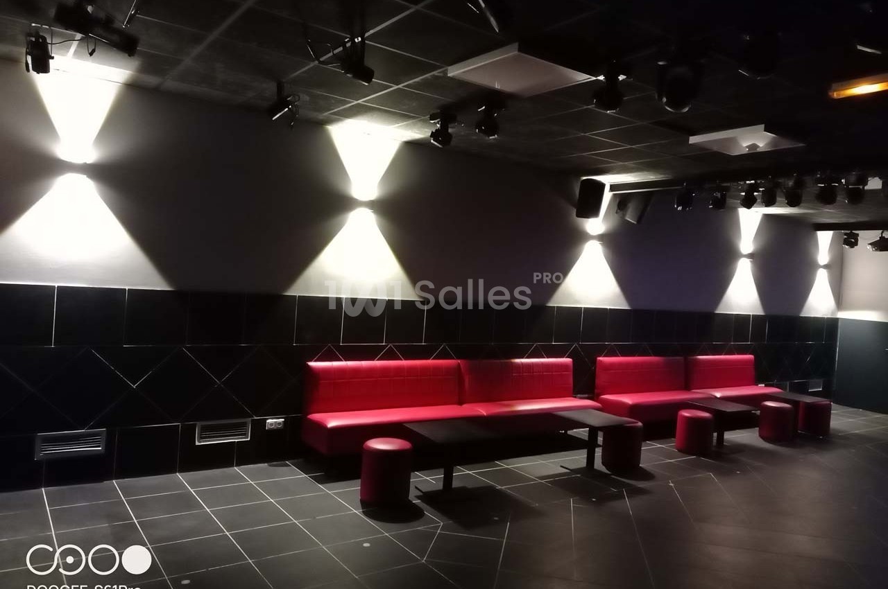 Salle sombre avec des banquettes rouges, des tabourets assortis et un éclairage mural dirigé vers le bas.