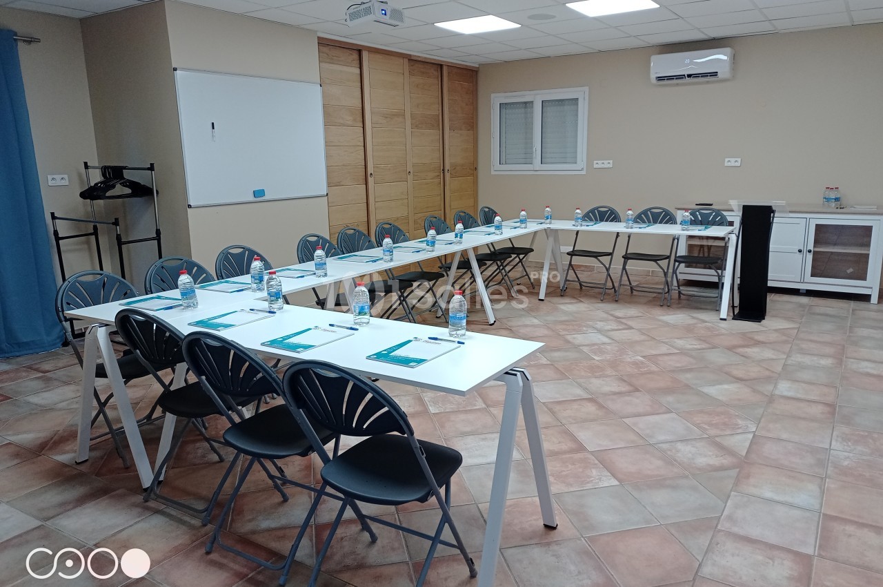 Salle de réunion équipée de tables disposées en U, chaises, bouteilles d'eau, paperboards et écran de projection.