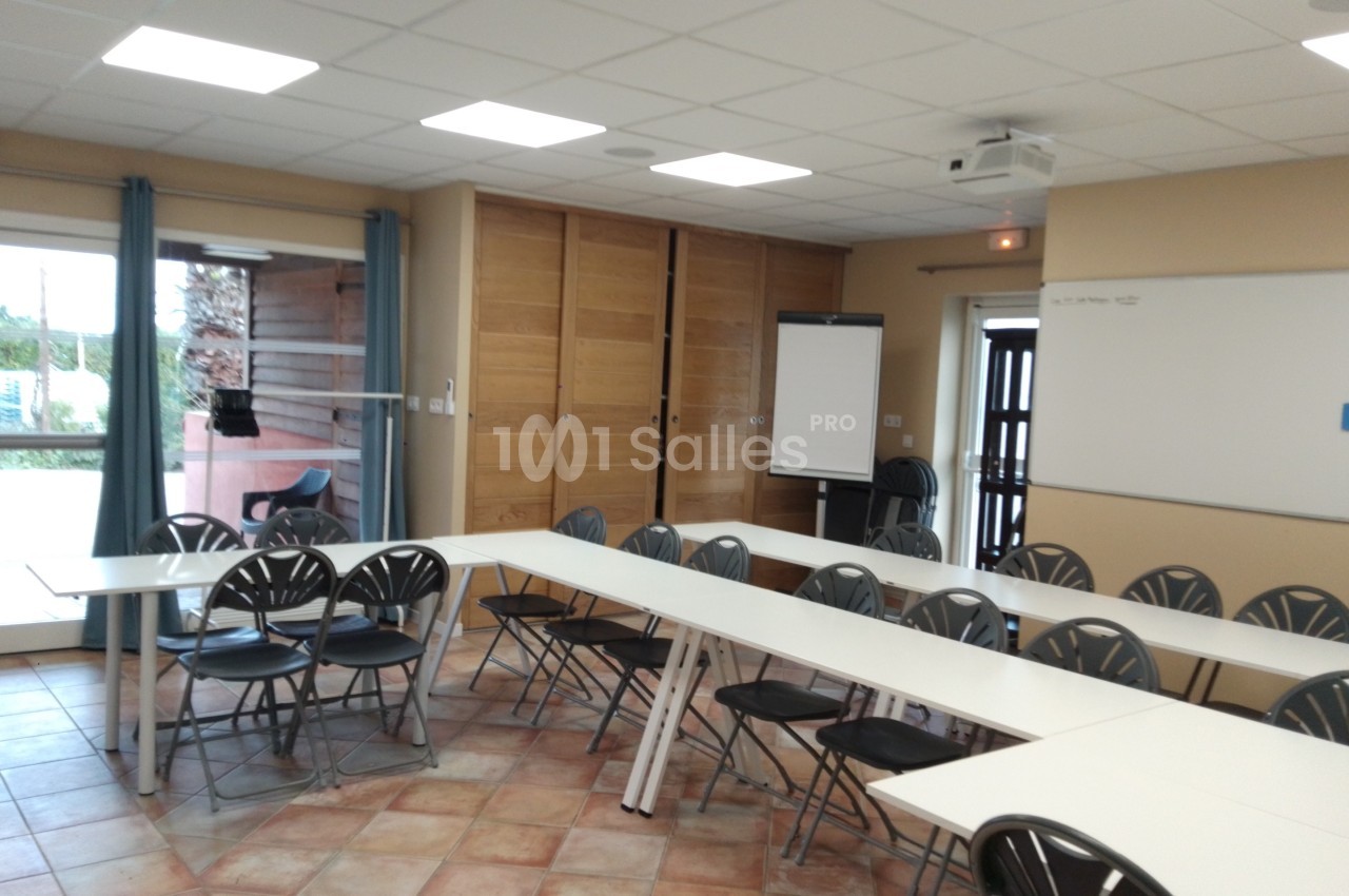 Salle de réunion lumineuse avec tables disposées en U, chaises noires, tableau blanc et paperboard.