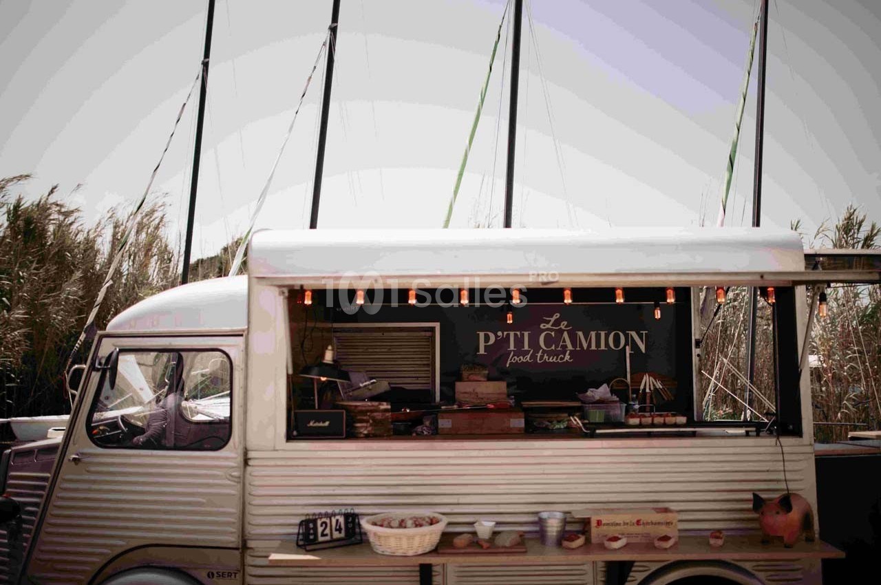 Food truck vintage stationné devant des roseaux et des mâts de bateau, avec une enseigne ’Le P'ti Camion’.
