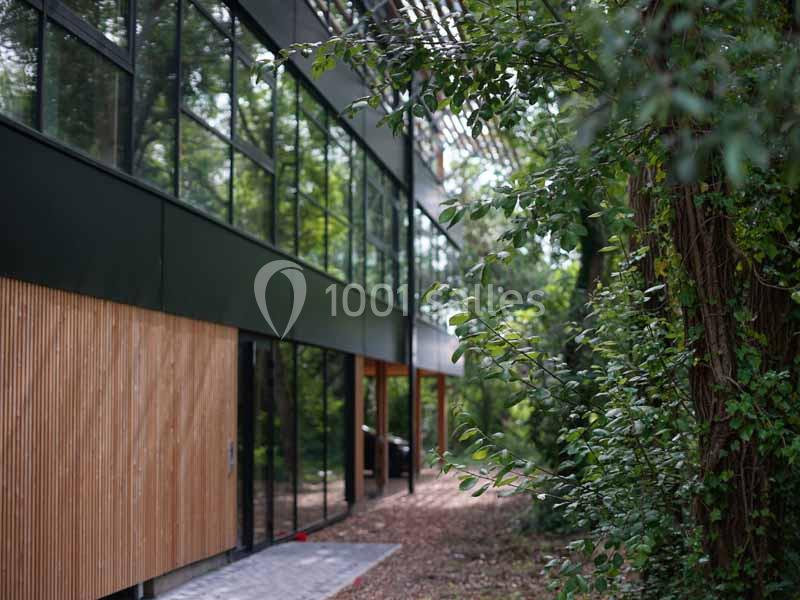 Bâtiment moderne avec façade vitrée et panneaux en bois, entouré de végétation dense.